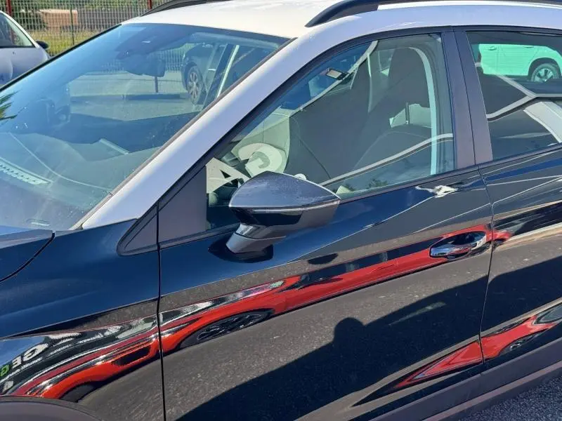 Vue latérale gauche du SEAT Arona noir Minuit Métal avec toit blanc Candy, mettant en valeur la portière et le rétroviseur.