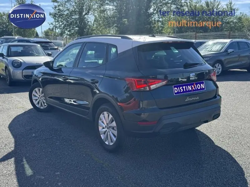 Vue 3/4 arrière droite d'un SEAT Arona noir Minuit Métal avec toit blanc Candy, stationné en extérieur sur parking.