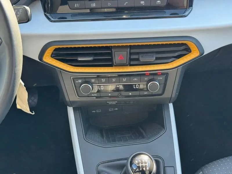 Vue intérieure centrée sur la console centrale du SEAT Arona 2025, avec cadre d'aération orange et levier de vitesses manuel.