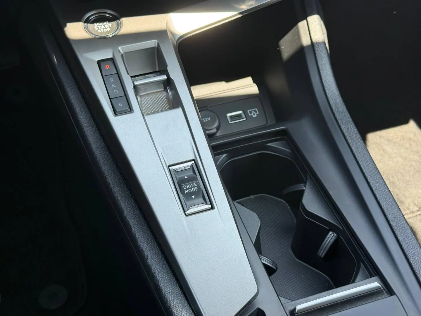 Vue en plongée sur la console centrale grise de la Peugeot e-308 2025 avec sélecteur de mode de conduite et prises USB/12V.