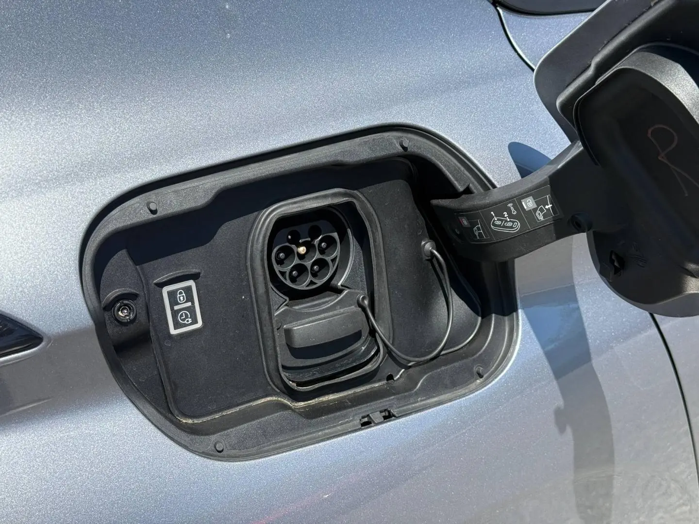 Prise de recharge électrique ouverte sur le côté gauche d’une Peugeot e-308 gris Artense métallisé.