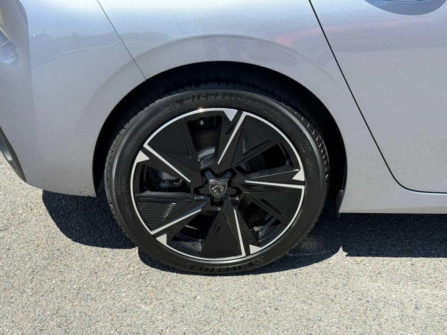 Gros plan sur la roue arrière droite d’une Peugeot e-308 gris Artense avec jante alu noire et argentée au design moderne.