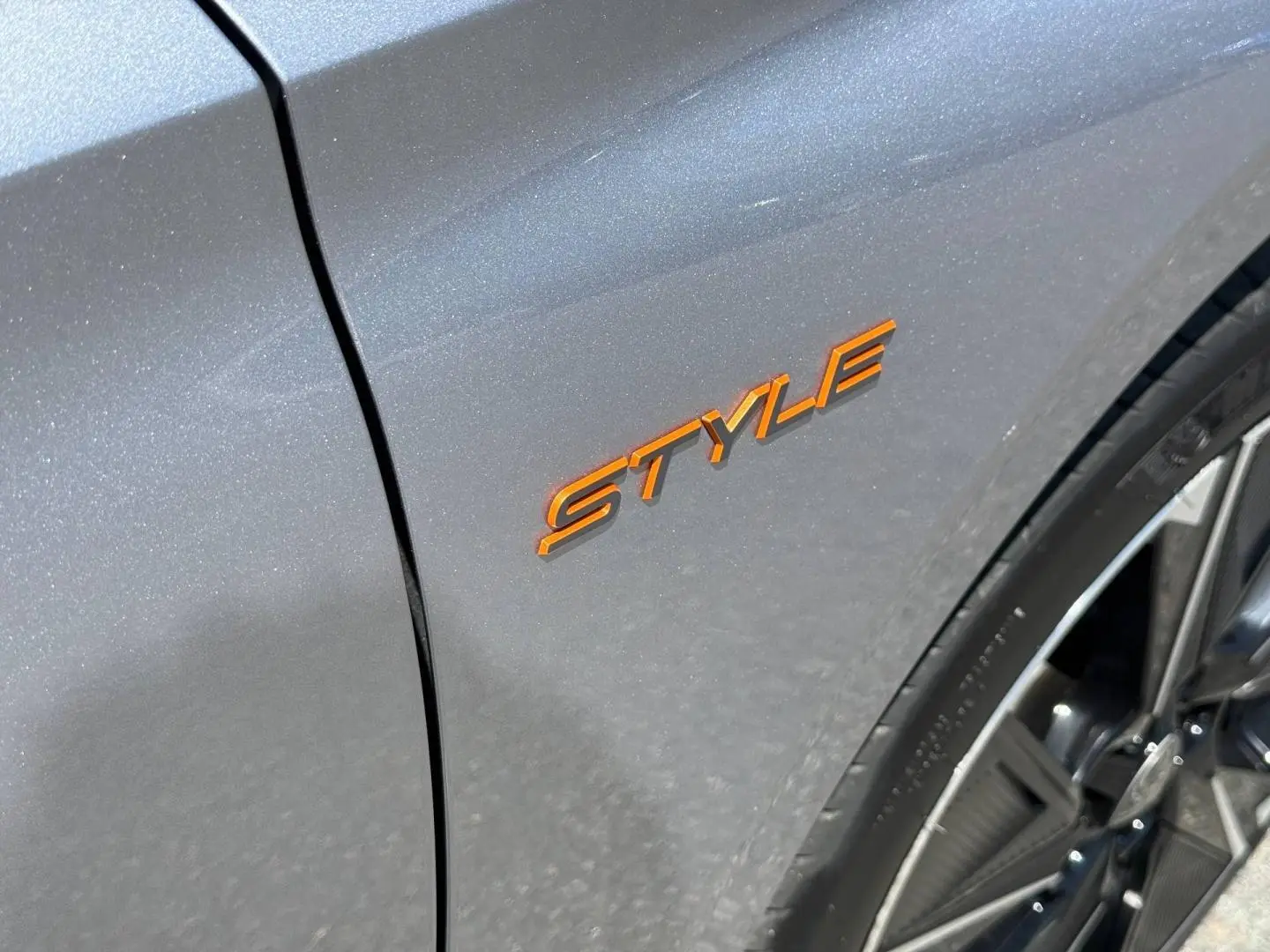 Gros plan sur l’aile avant droite gris Artense avec logo Style orange et jante alu visible.