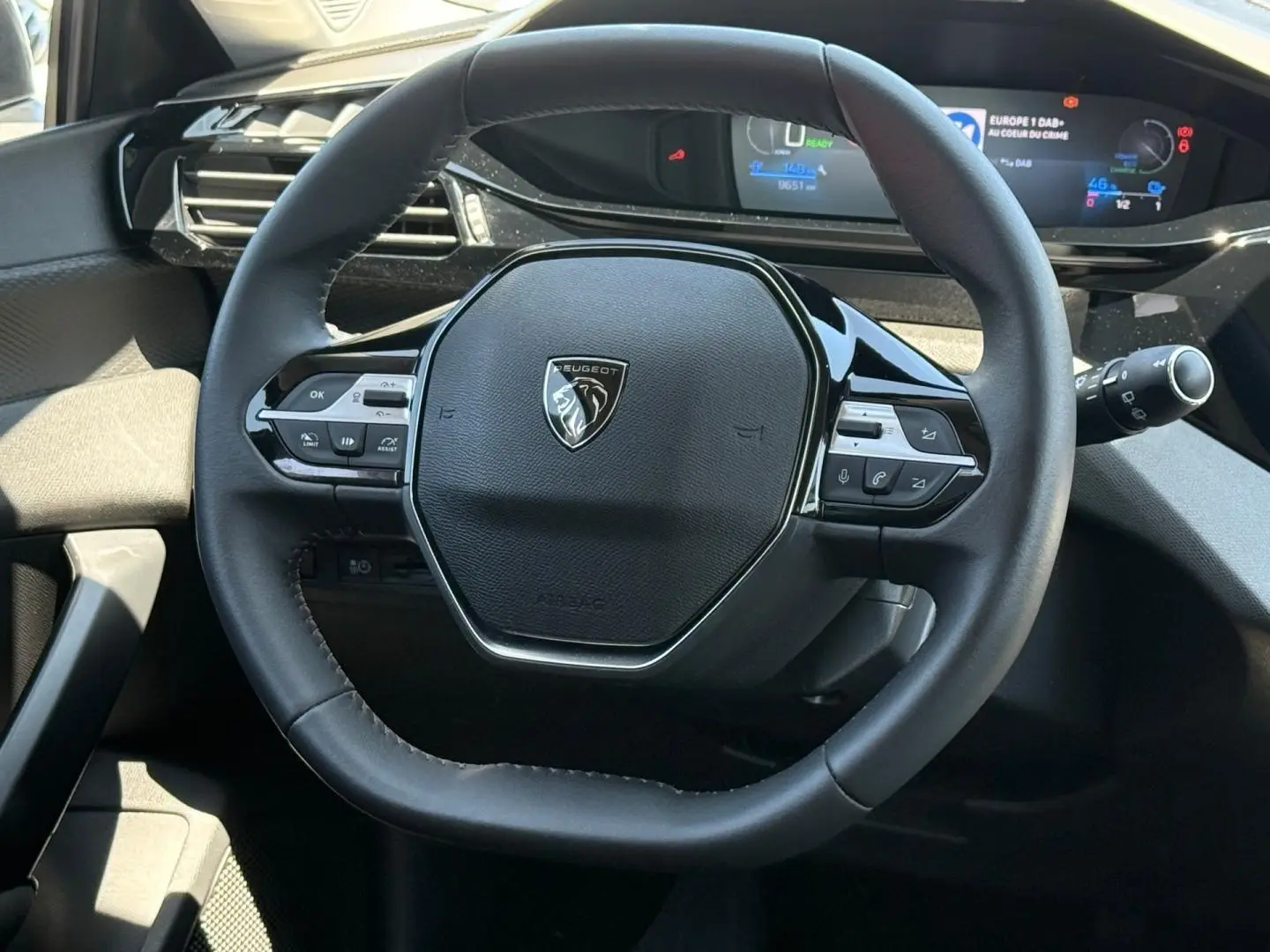 Vue rapprochée du volant multifonction noir de la Peugeot e-308 2025 avec tableau de bord numérique en arrière-plan.