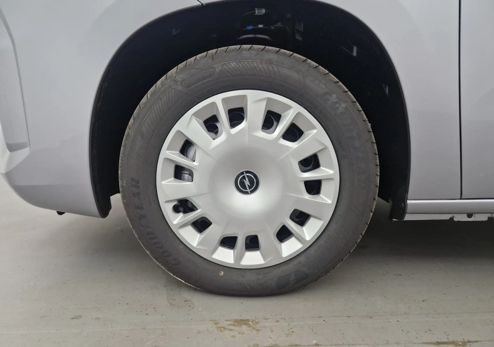 Gros plan sur la roue avant gauche grise d'un Opel Combo Life avec jante en plastique et logo central Opel.