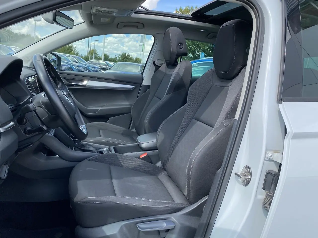Intérieur côté conducteur d'un Skoda Karoq blanc avec sièges noirs et toit ouvrant panoramique en verre.
