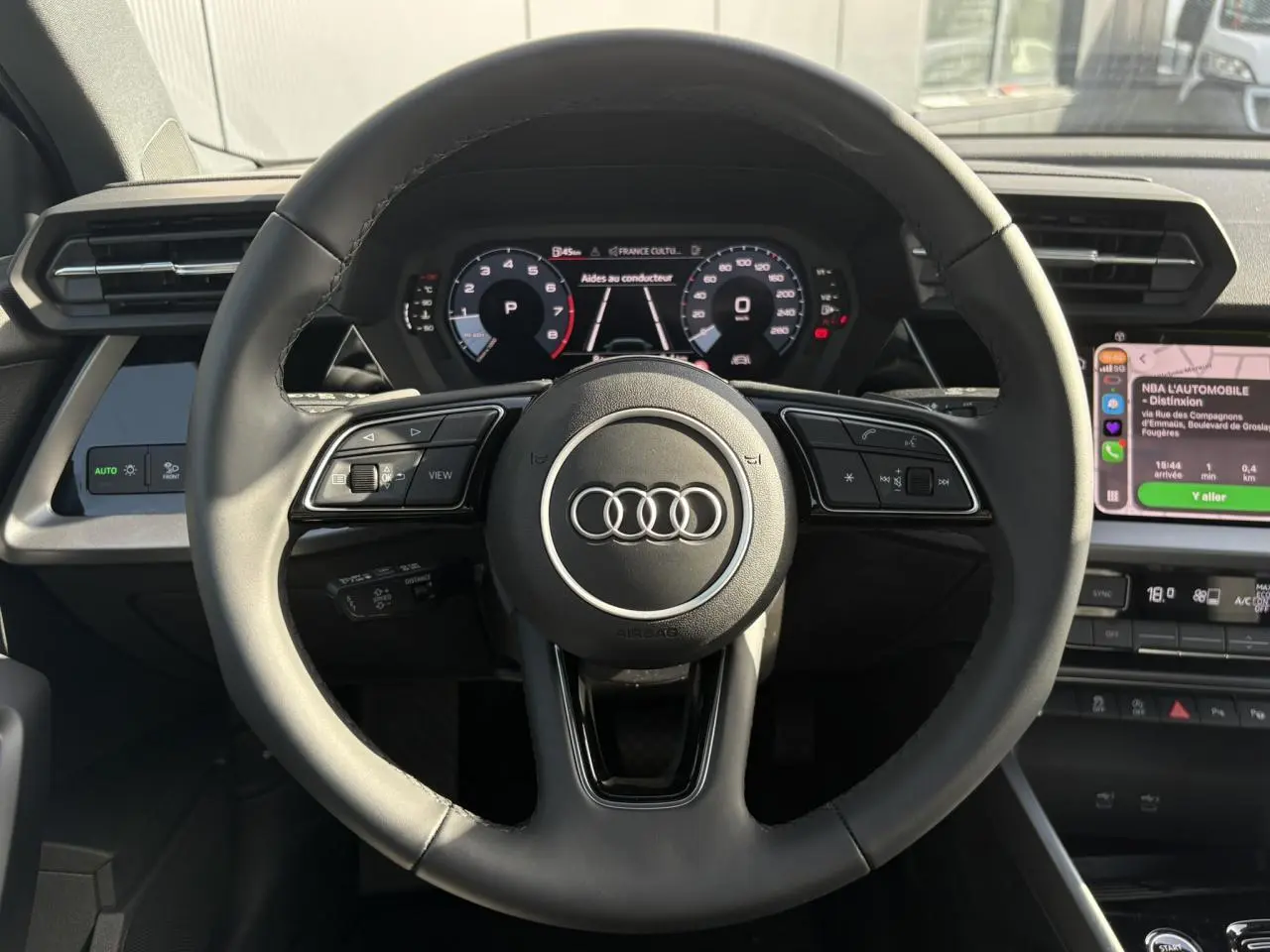 Vue intérieure centrée sur le volant cuir noir multifonctions de l'Audi A3 Berline 2024 avec tableau de bord digital.