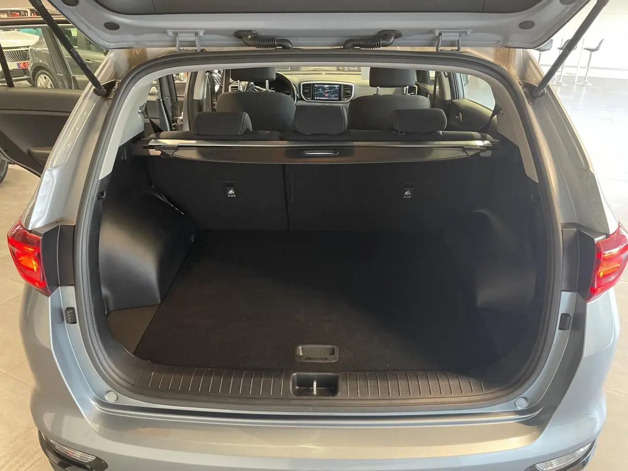 Coffre ouvert vu de l'arrière d'un KIA Sportage gris clair 2021 avec intérieur noir et tablette de coffre.