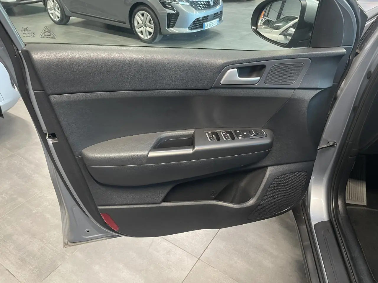 Porte avant gauche ouverte du Kia Sportage gris clair 2021, avec commandes électriques et haut-parleur intégré.