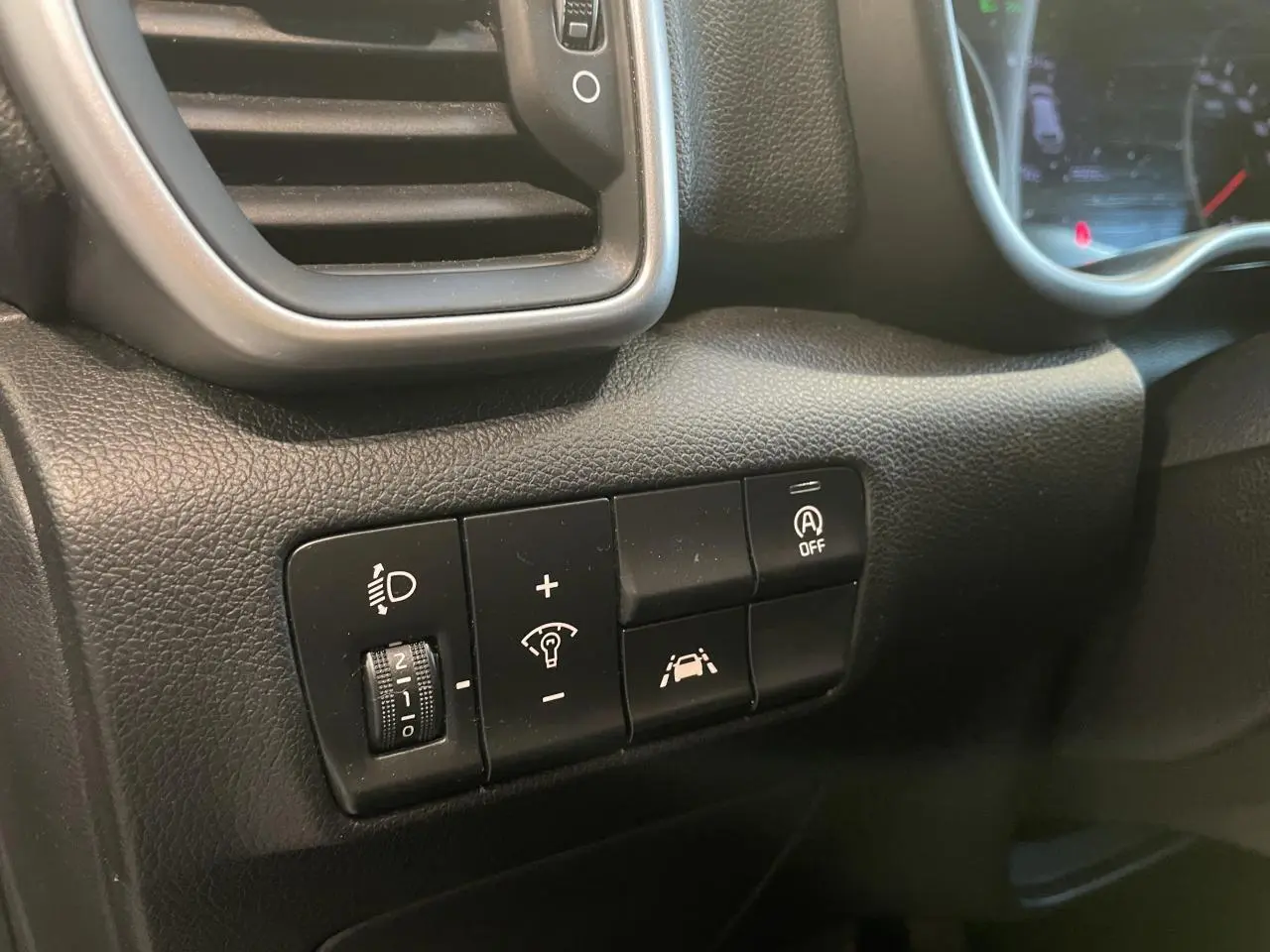 Gros plan sur les commandes noires du tableau de bord du Kia Sportage gris clair, côté gauche du conducteur.