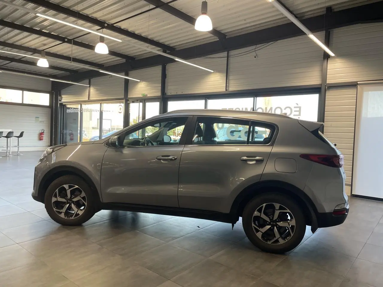 Vue de profil côté gauche d'un Kia Sportage gris clair 2021 en showroom avec jantes alliage 16 pouces.