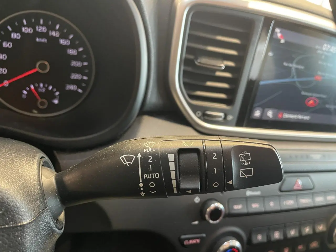 Gros plan sur la commande des essuie-glaces dans l’habitacle noir du Kia Sportage gris clair, avec écran tactile en arrière-plan.