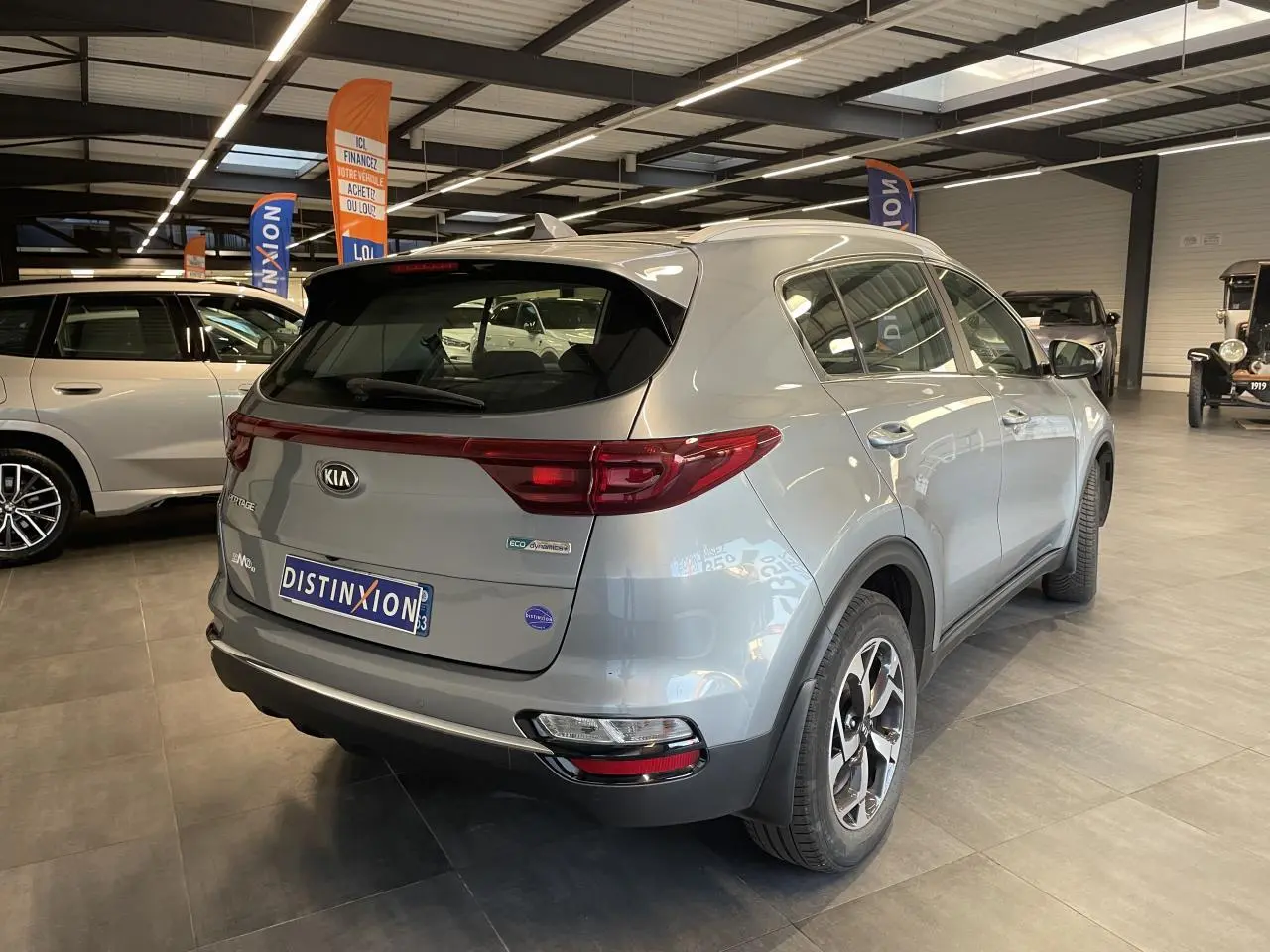 Vue 3/4 arrière droite du KIA Sportage gris clair métallisé en showroom avec jantes alliage et becquet arrière intégré.