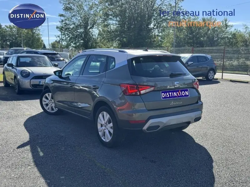 Vue 3/4 arrière droite d'un SEAT Arona noir avec barres de toit et jantes alu sur parking ensoleillé.