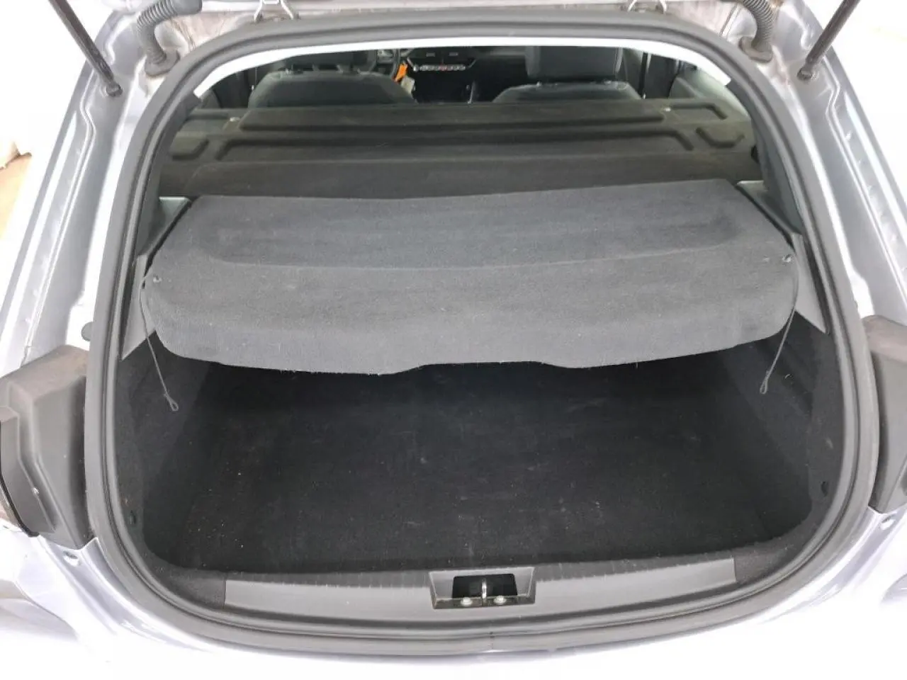 Coffre ouvert vu de l'arrière d'une Peugeot 208 gris Artense avec cache-bagages noir relevé.