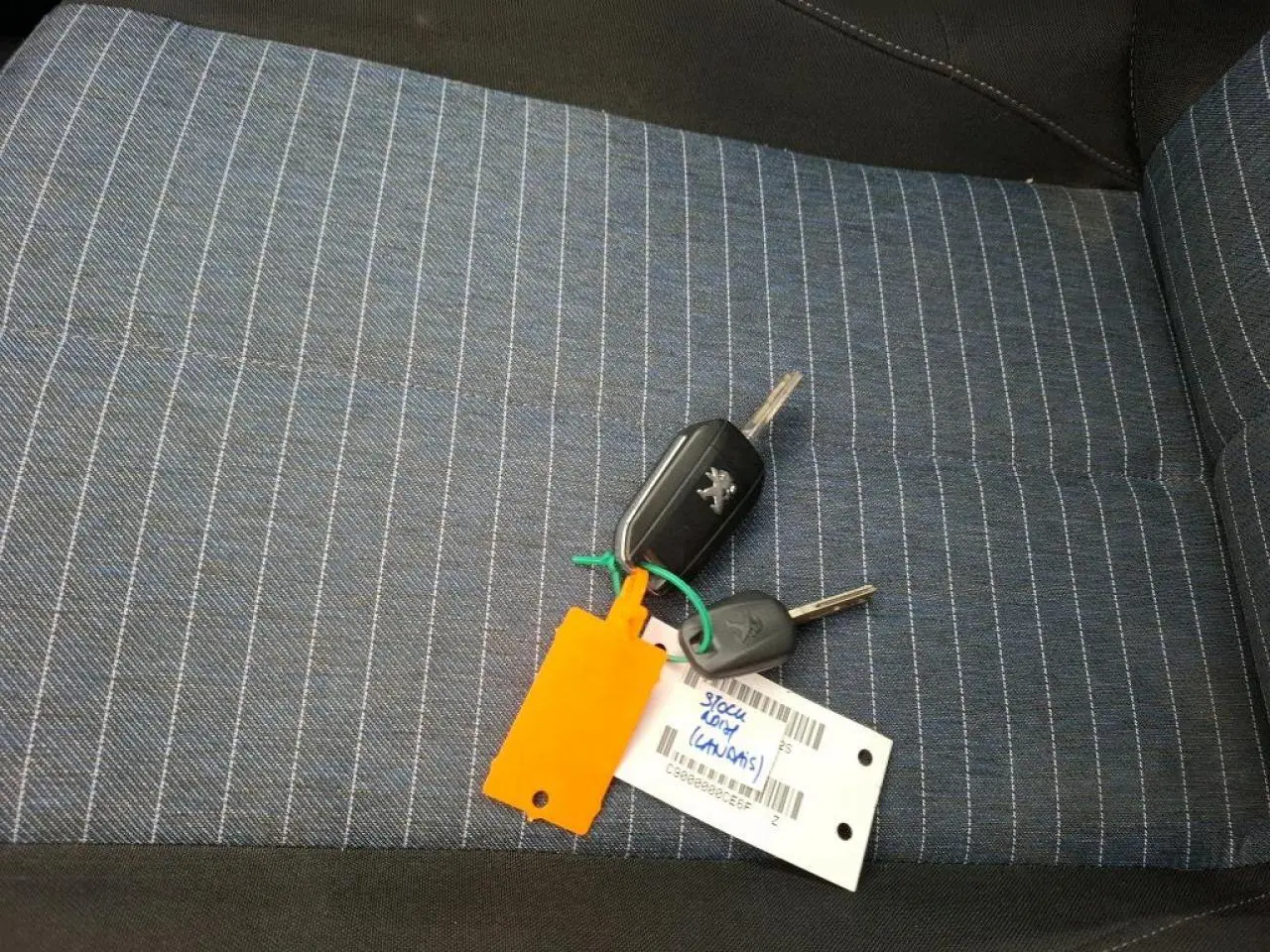 Clé Peugeot posée sur siège tissu bleu à rayures grises, intérieur d’une Peugeot 208 1.2i 2021.