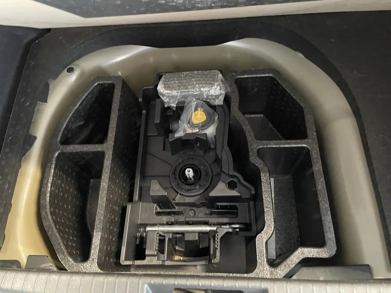 Compartiment de rangement sous coffre de la Peugeot 208 gris Artense, avec kit de dépannage pneumatique rangé.