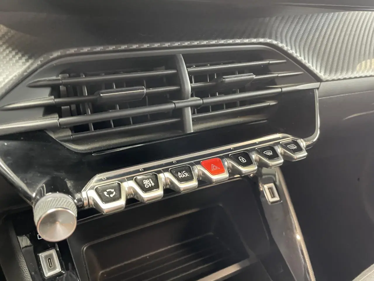 Gros plan sur la console centrale noire brillante de la Peugeot 208 avec rangements et boutons de commande alignés.