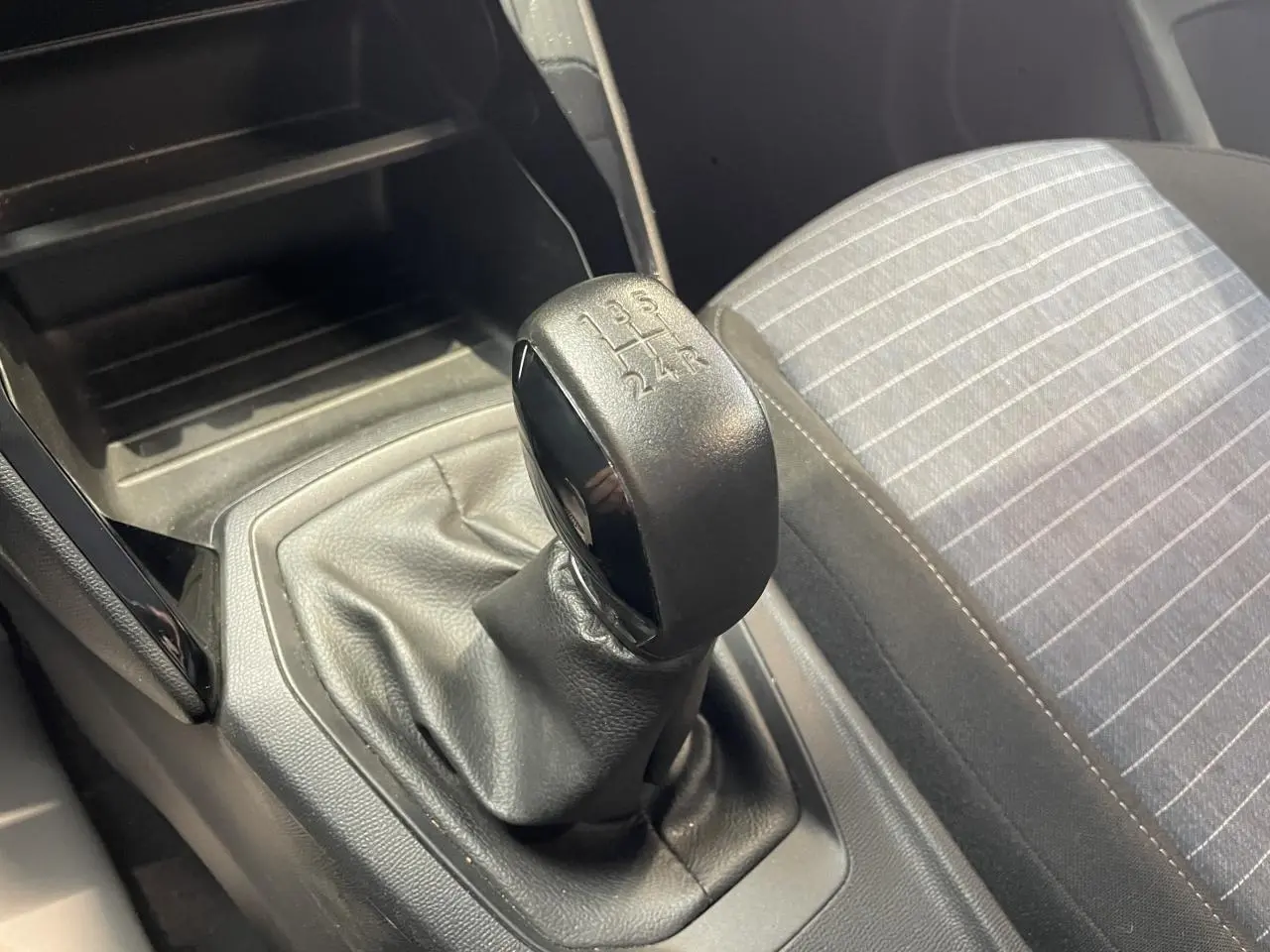 Gros plan sur le levier de vitesses manuel noir et la sellerie tissu gris à rayures de la Peugeot 208.