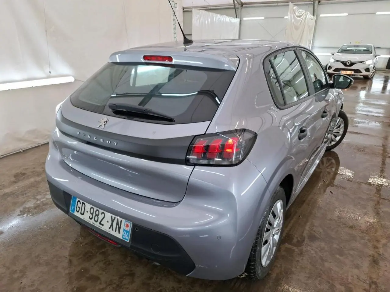 Vue 3/4 arrière droite d'une Peugeot 208 gris Artense avec feux arrière allumés en intérieur.