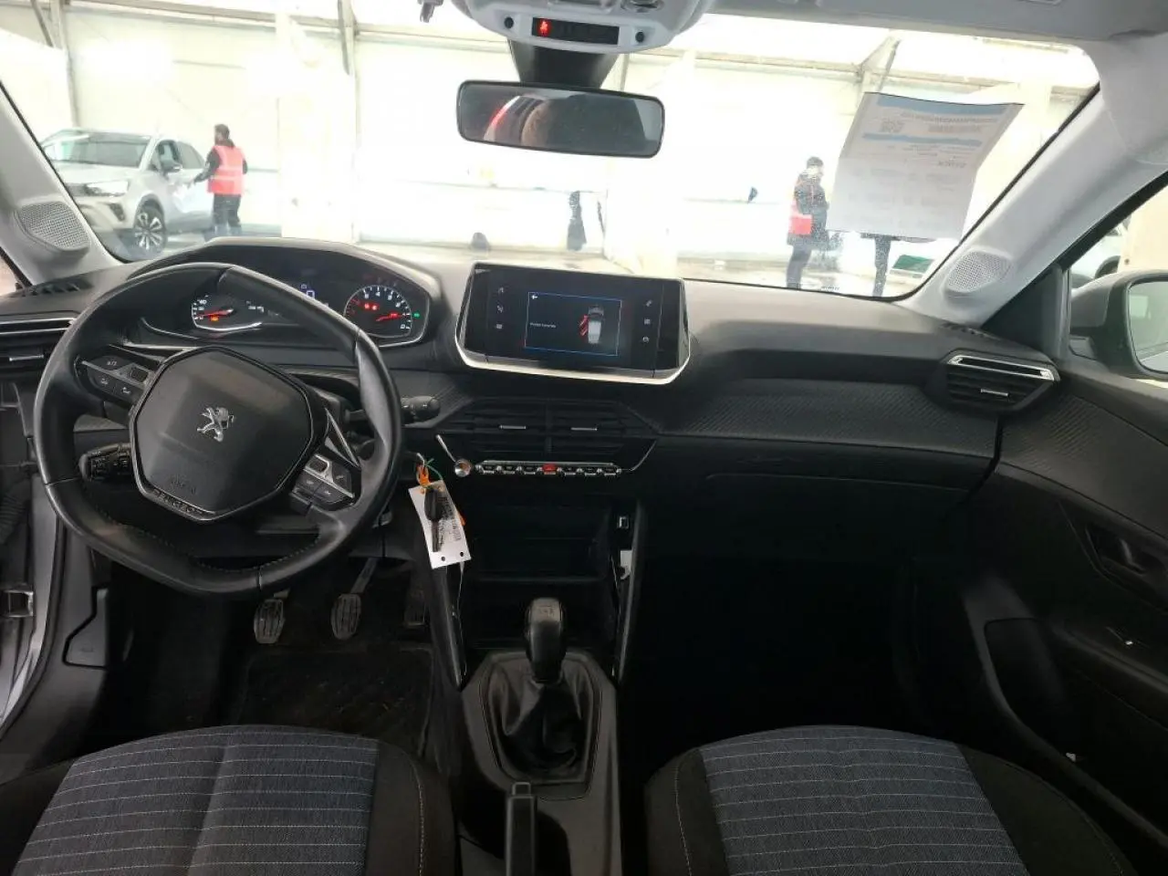 Vue intérieure avant de la Peugeot 208 1.2i 12V avec tableau de bord noir et volant compact au centre.