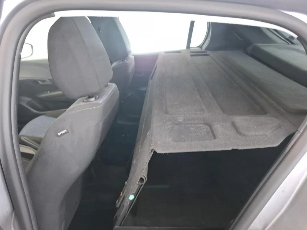 Vue intérieure arrière droite d'une Peugeot 208 gris Artense avec banquette rabattue et cache-bagages noir.