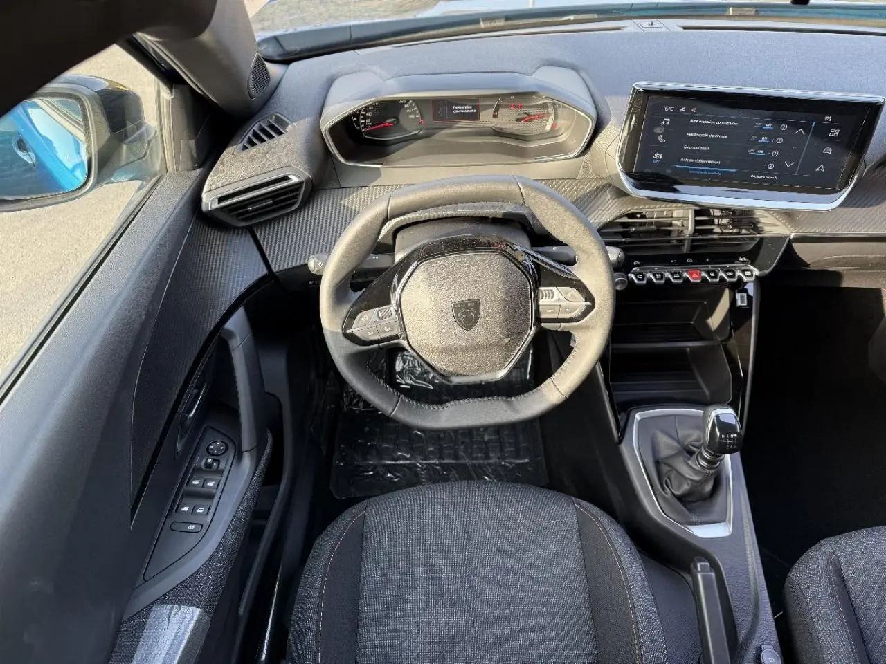Vue intérieure du poste de conduite du Peugeot 2008 2025, volant compact, écran tactile et levier de vitesse manuel visibles.