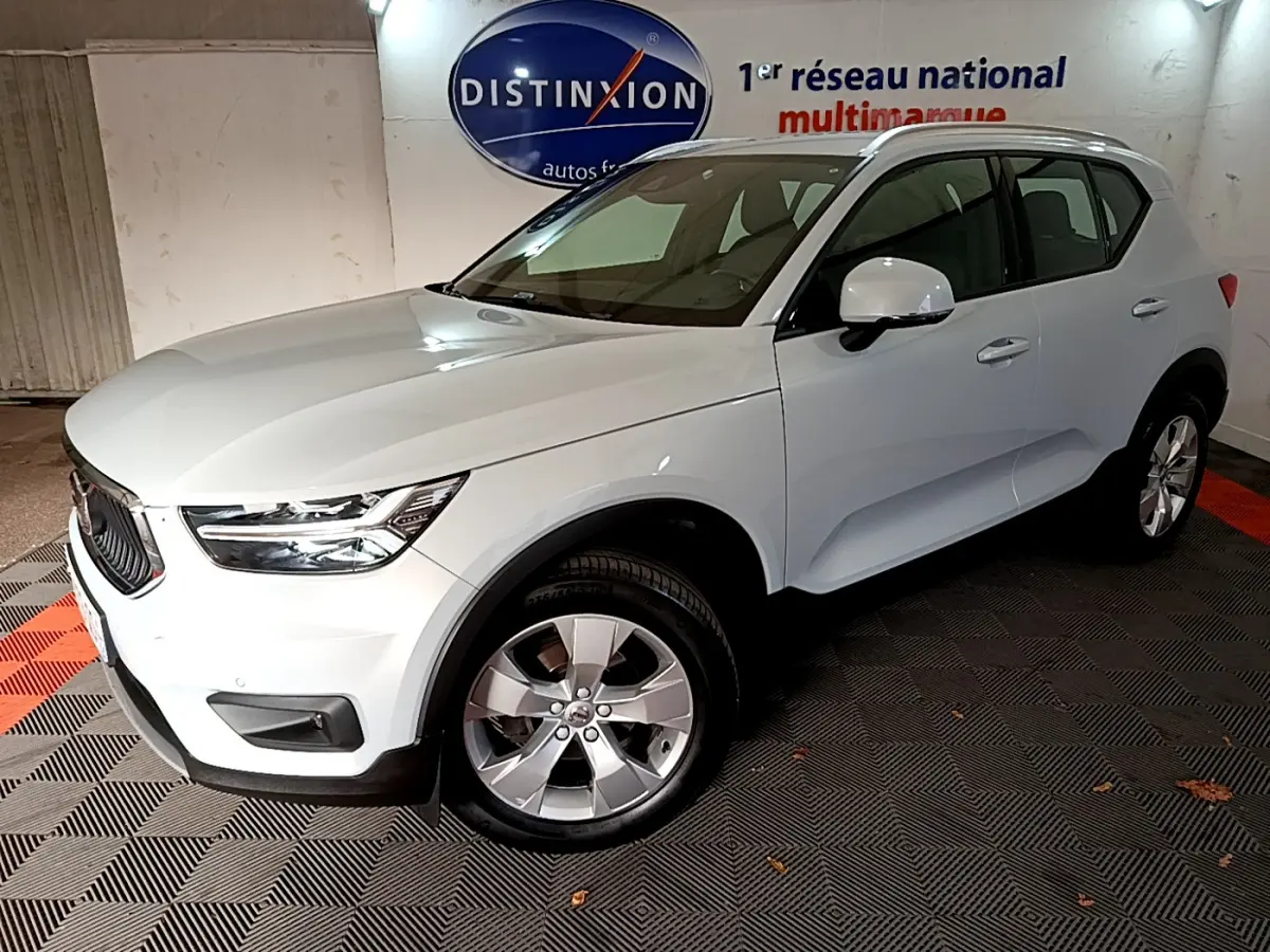 Vue 3/4 avant d'un Volvo XC40 gris clair garé en intérieur avec jantes alliage et calandre noire distinctive.