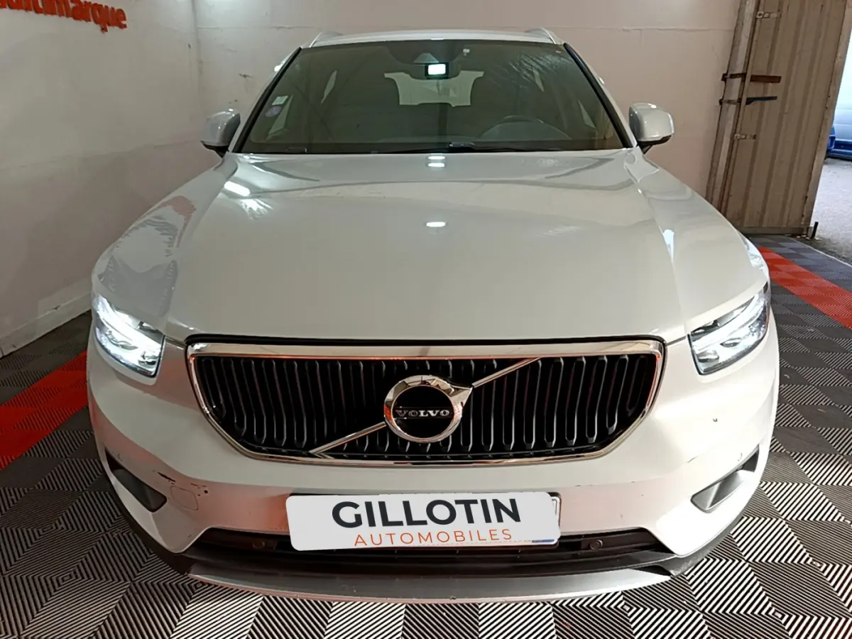 Vue frontale d'un Volvo XC40 gris clair avec calandre noire et phares LED allumés dans un garage.