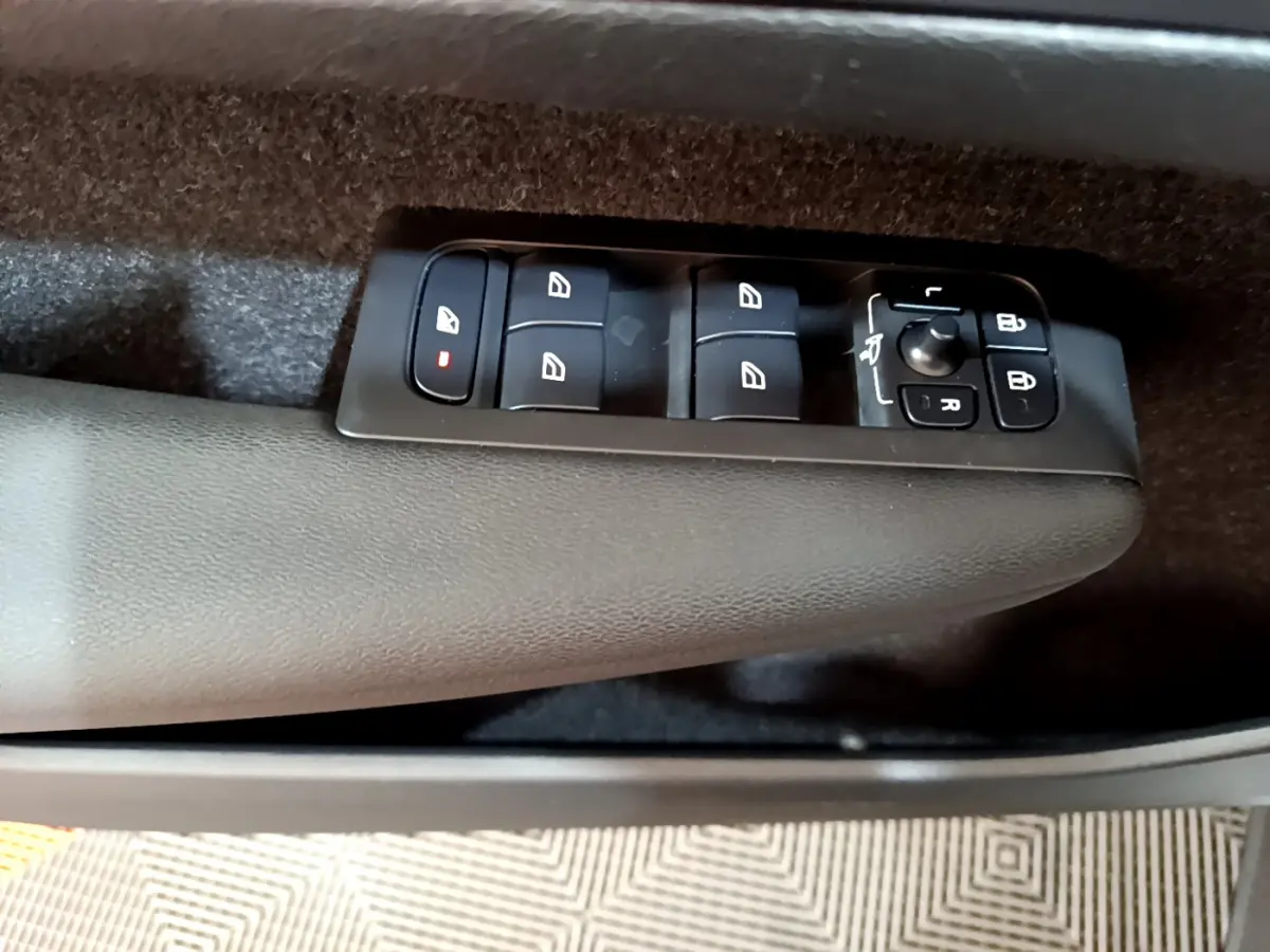Gros plan sur les commandes des vitres et rétroviseurs sur la porte côté conducteur du Volvo XC40 gris clair.