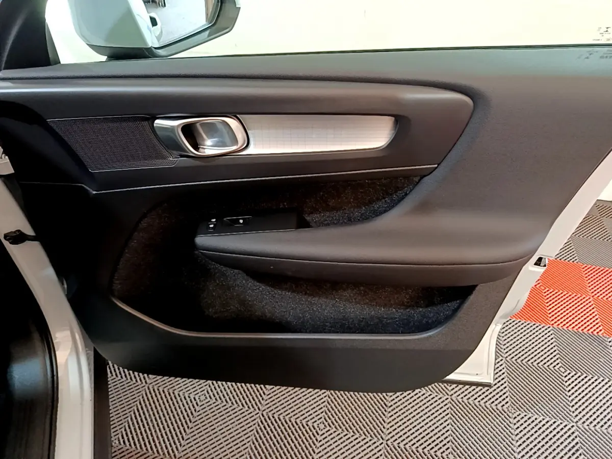 Intérieur montrant la porte côté gauche du Volvo XC40 gris clair avec poignée argentée et commandes de vitres.