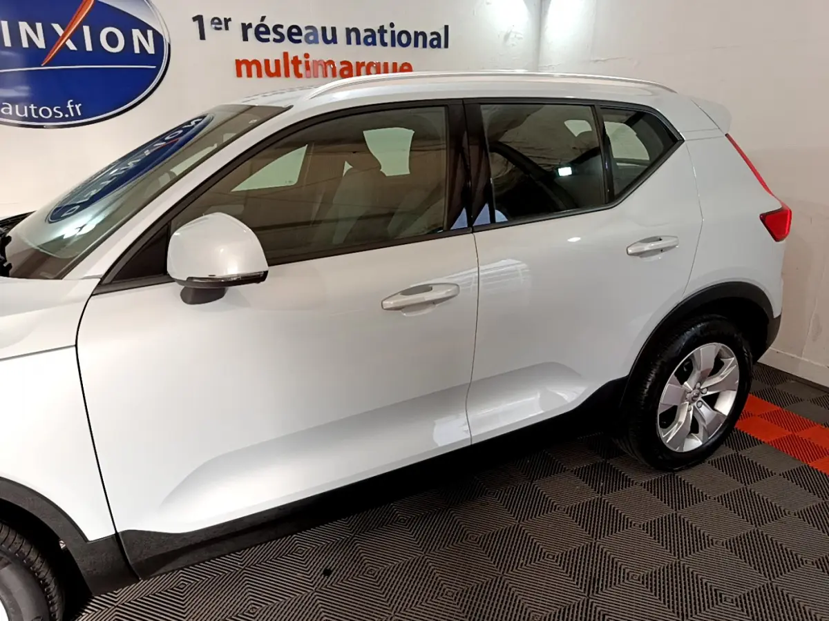 Profil côté gauche d'un Volvo XC40 gris clair 2020 avec jantes alliage et rétroviseurs blancs dans un showroom.