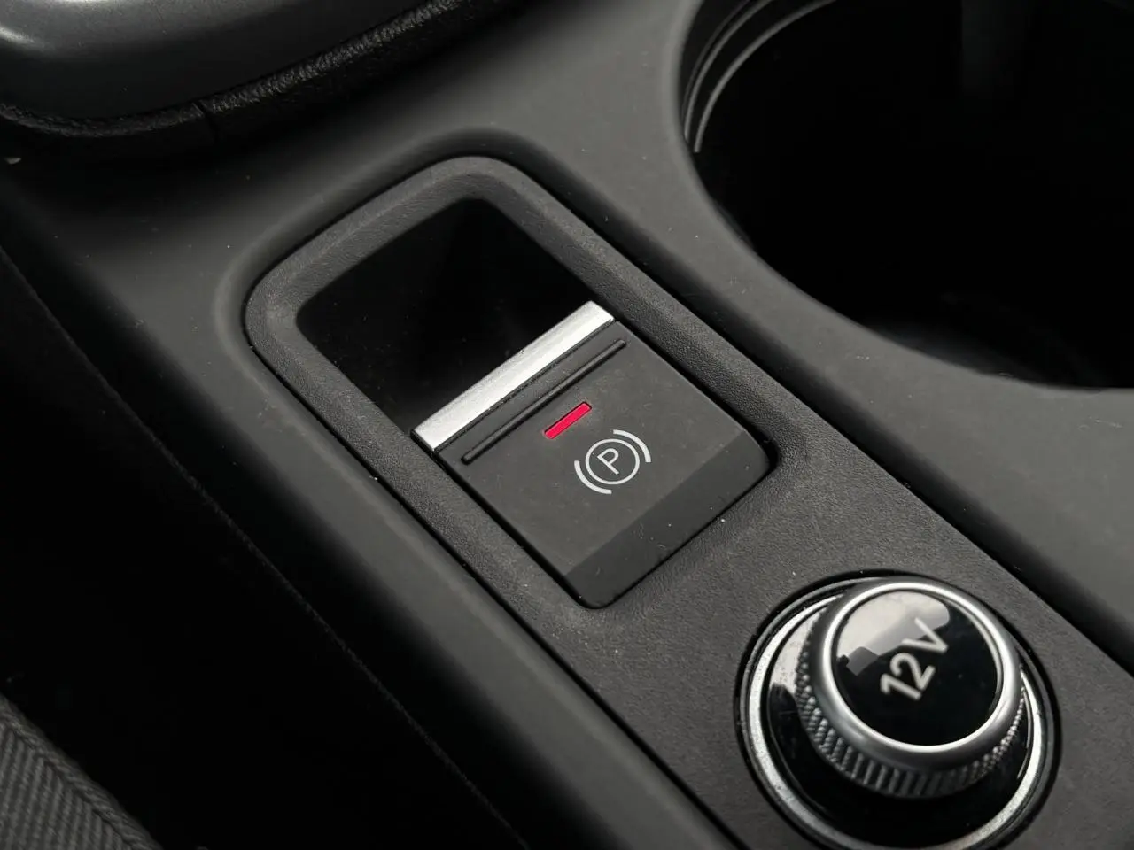 Gros plan sur le bouton de frein à main électronique et prise 12V dans la console centrale d'une Audi A3 Berline 2024.