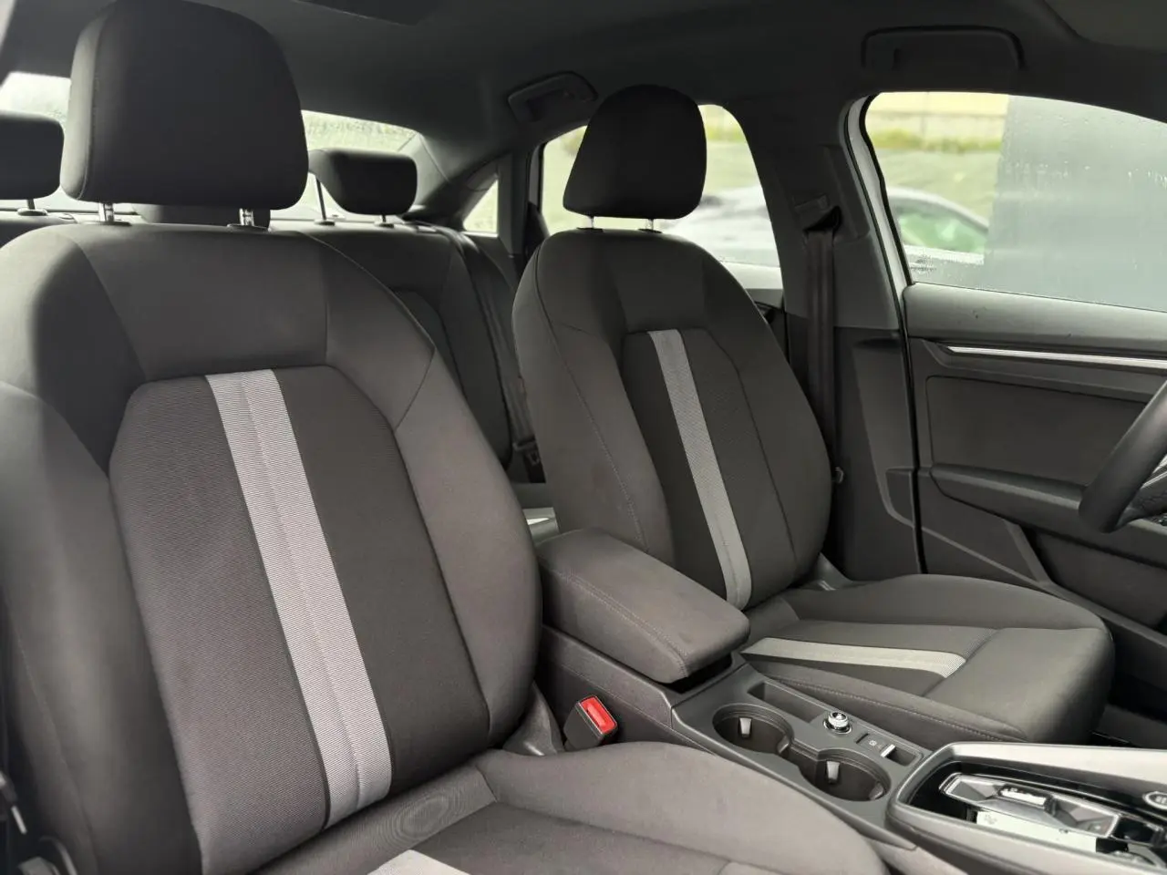 Vue intérieure montrant les sièges avant gris avec bande centrale claire et accoudoir coulissant de l'Audi A3 Berline 2024.