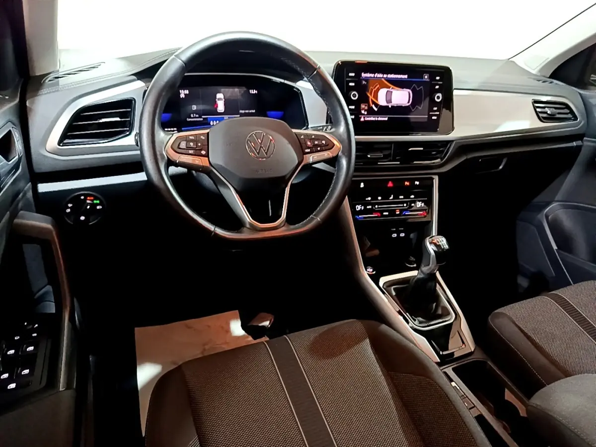 Vue intérieure avant du Volkswagen T-Roc gris foncé 2022, volant cuir, écran tactile et levier de vitesse manuel visibles.