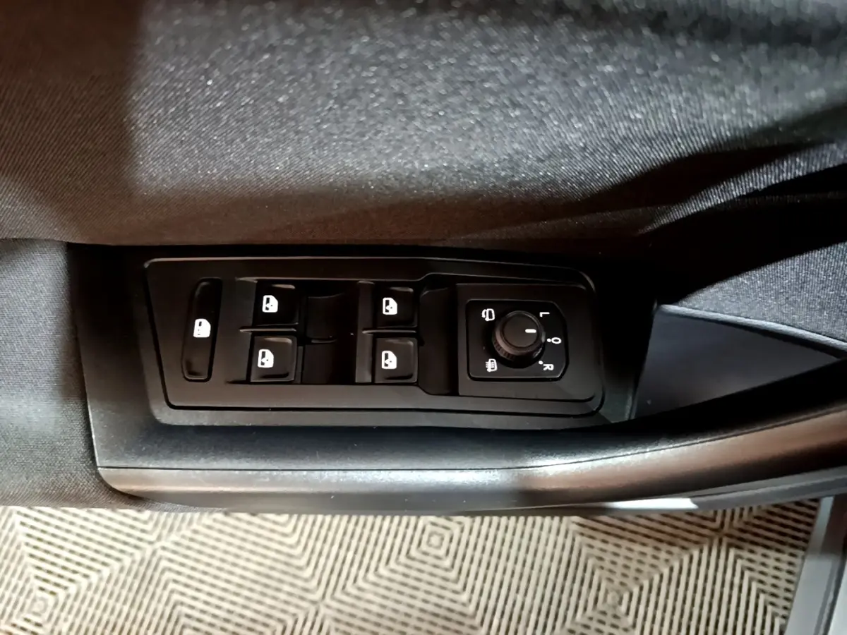 Vue rapprochée des commandes de lève-vitres et réglage des rétroviseurs côté conducteur d’un Volkswagen T-Roc gris foncé.