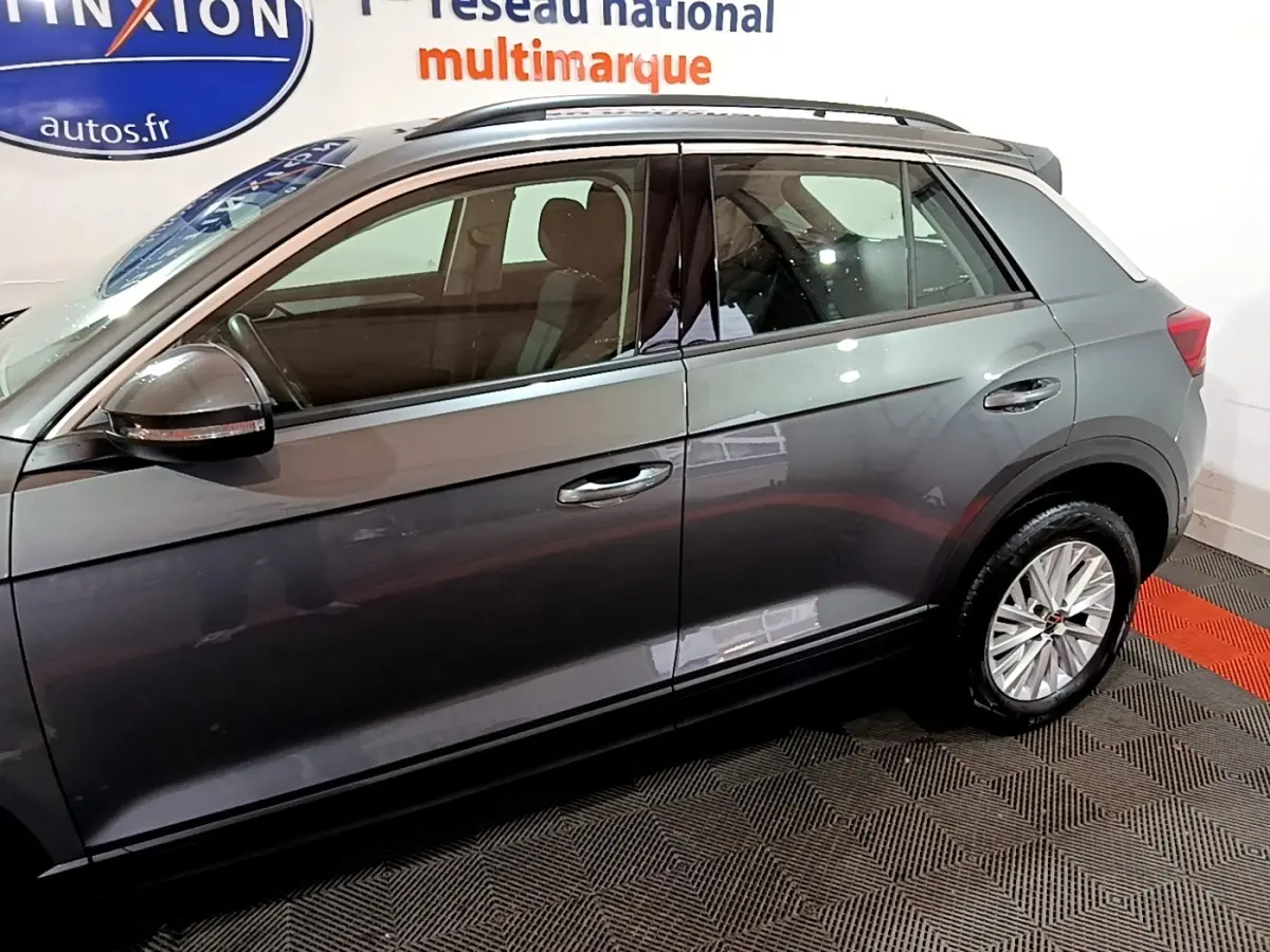 Vue latérale côté gauche du Volkswagen T-Roc gris foncé 2022, mettant en valeur les jantes et la ligne de toit chromée.