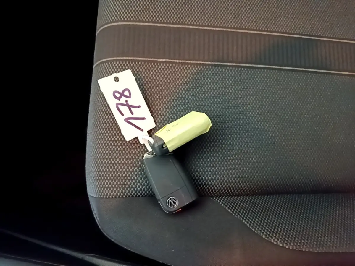 Clé noire Volkswagen posée sur la banquette arrière en tissu gris foncé à motifs, vue en plongée rapprochée.