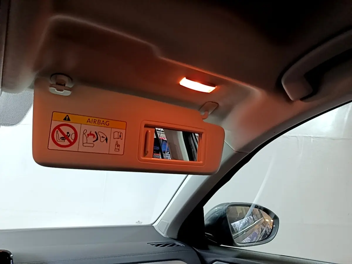 Vue intérieure côté passager du pare-soleil beige avec miroir et rétroviseur extérieur noir visible sur un Volkswagen T-Roc gris foncé.