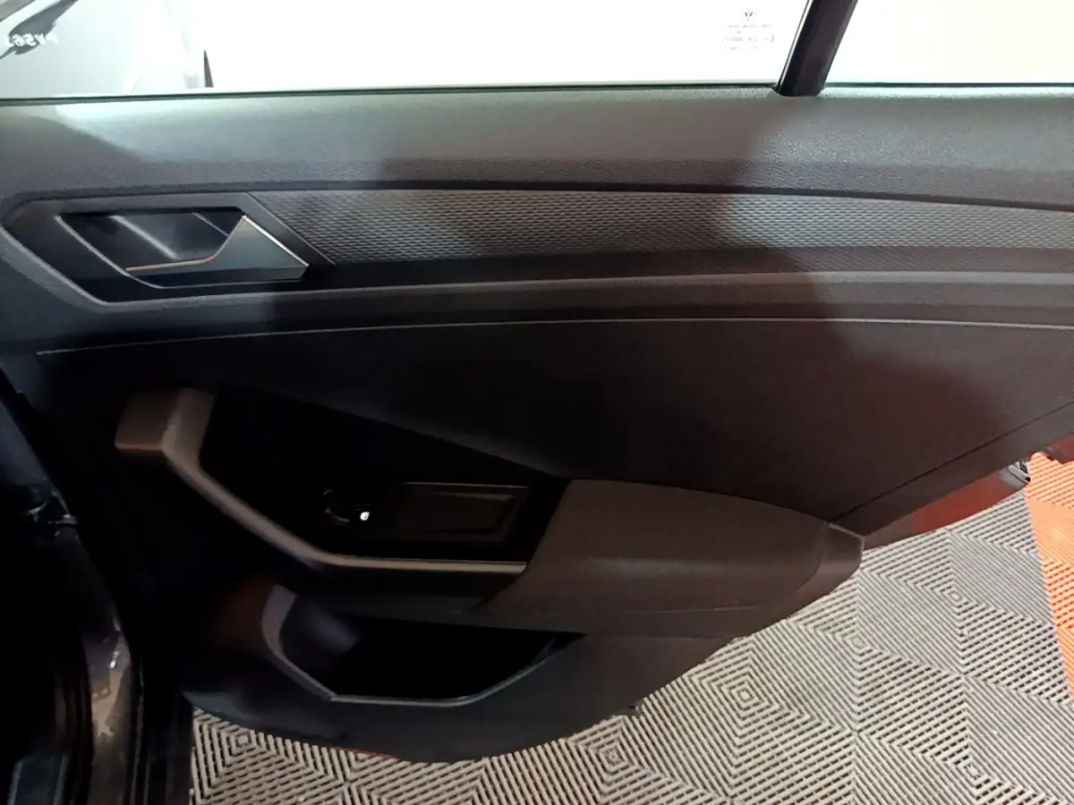 Vue intérieure de la porte côté gauche du Volkswagen T-Roc gris foncé, avec poignée et commande de vitre.