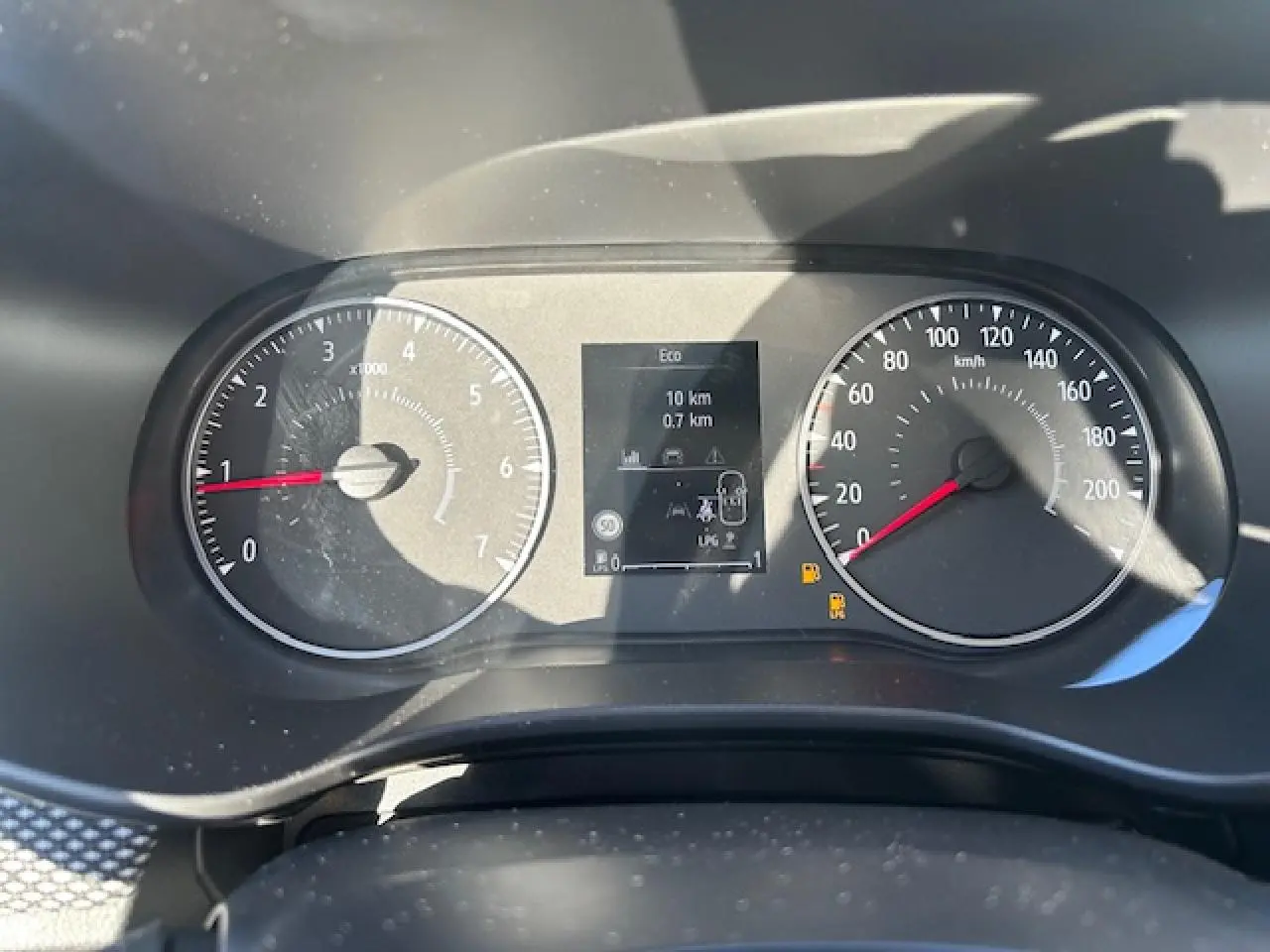 Vue rapprochée du tableau de bord numérique et compteurs analogiques de la Dacia Sandero blanche, affichant la vitesse et le régime moteur.