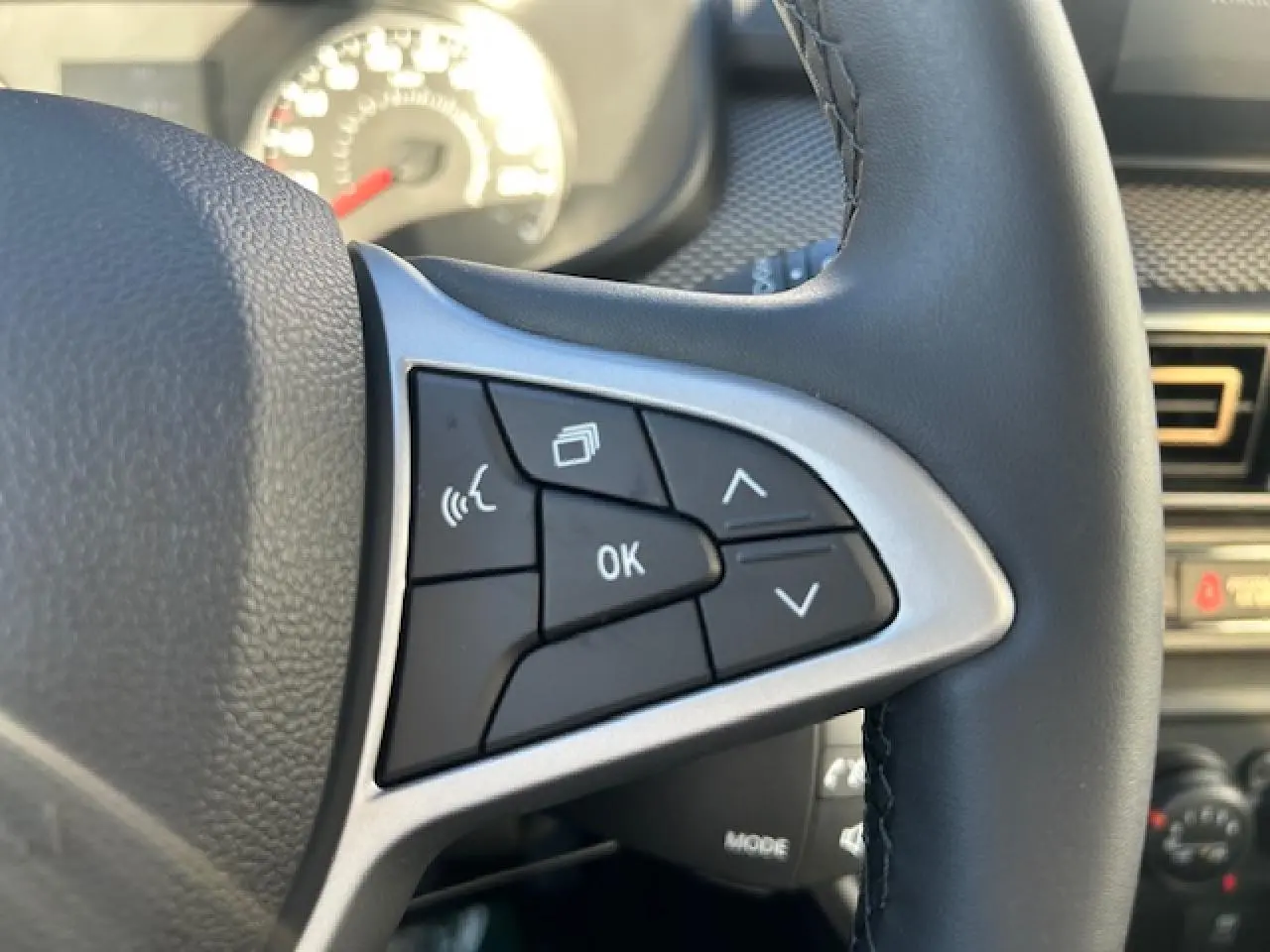 Gros plan sur les commandes au volant côté droit du Dacia Sandero Stepway blanc, avec boutons multifonctions et finition argentée.