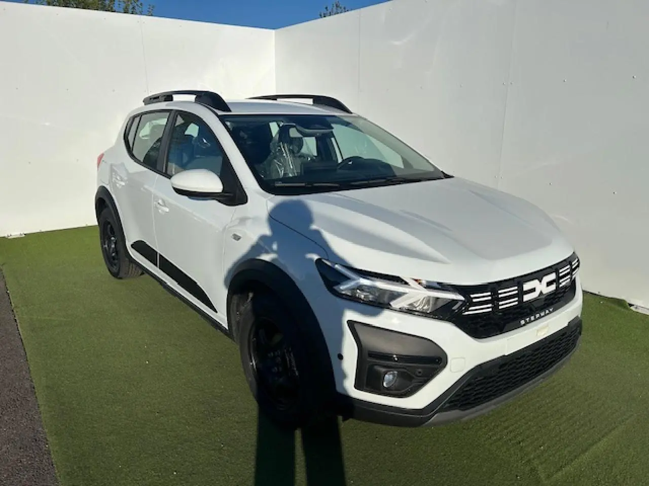 Dacia Sandero Stepway blanc arctique vue 3/4 avant droit avec barres de toit noires et signature lumineuse LED.