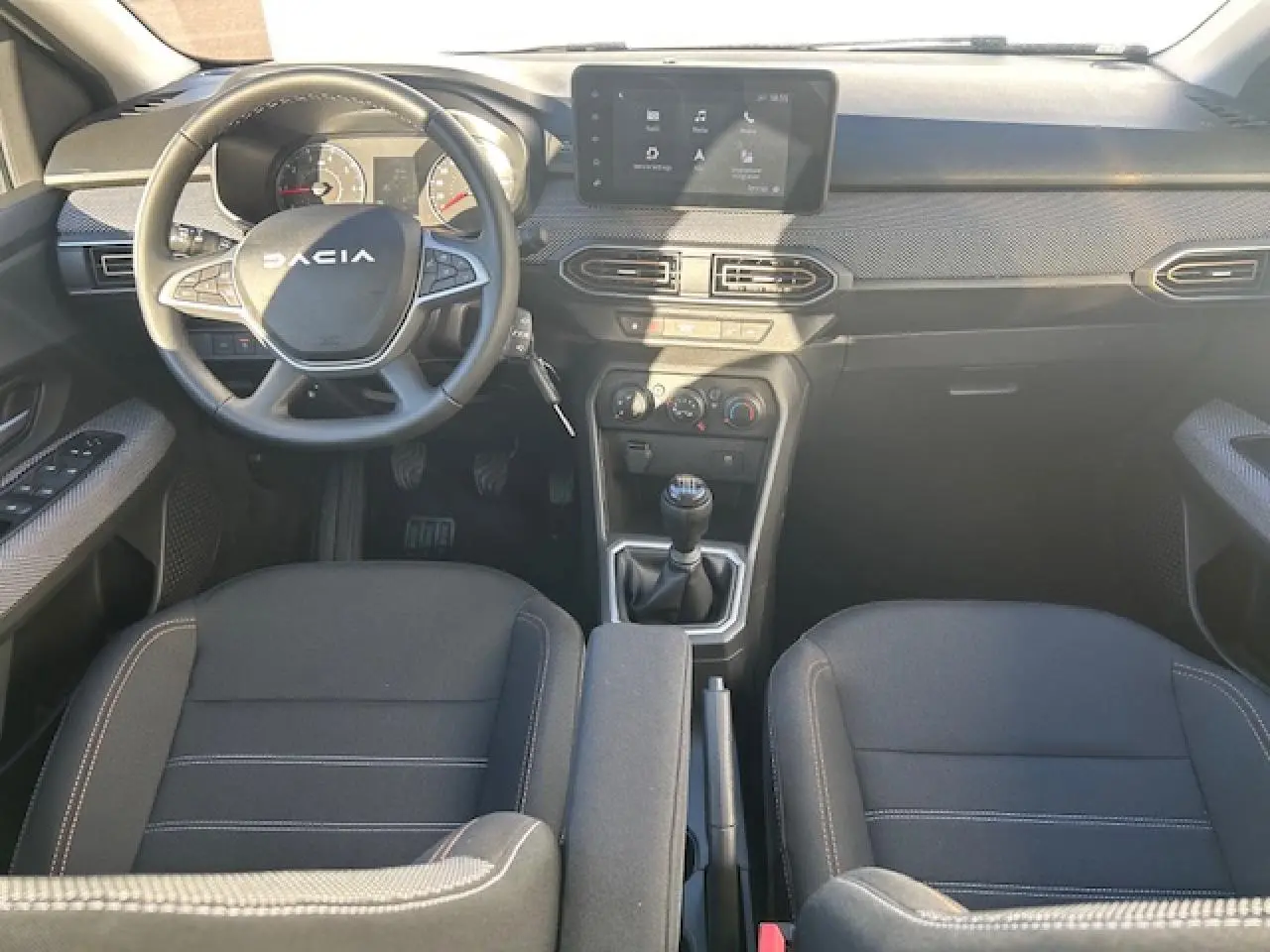 Vue intérieure avant centrée sur le tableau de bord et volant noir de la Dacia Sandero Stepway 2025 avec écran tactile 8 pouces.