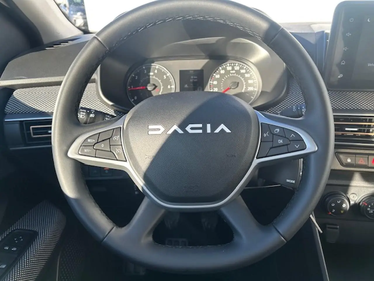 Vue rapprochée du volant noir de la Dacia Sandero Stepway 2025 avec commandes intégrées et tableau de bord numérique.