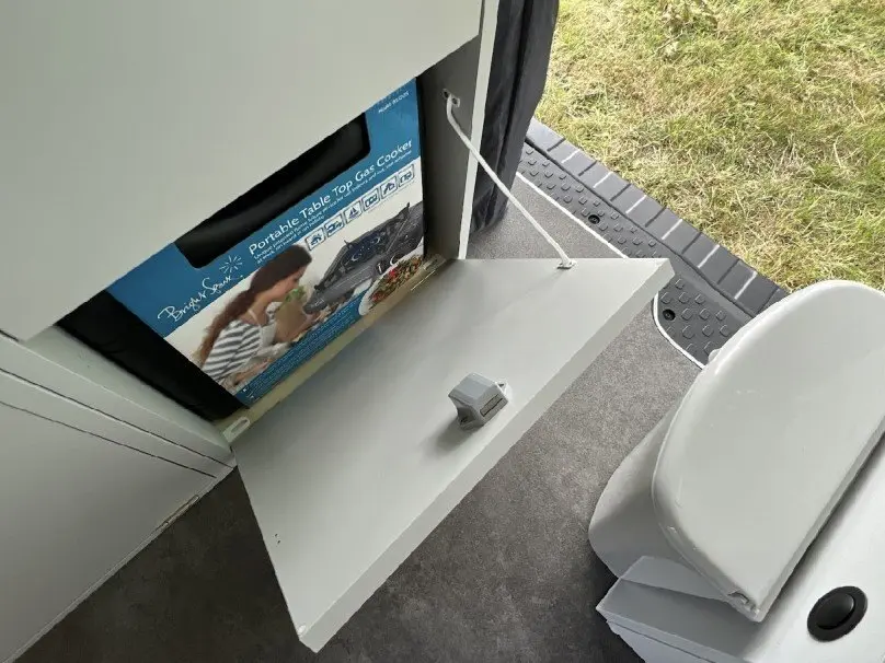 Vue intérieure du fourgon aménagé Renault Trafic gris, montrant une table rabattable et une prise électrique près de la porte ouverte.