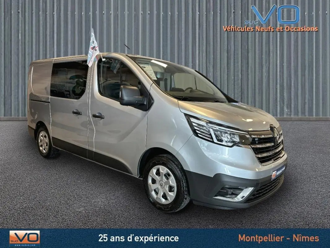 Vue 3/4 avant d’un Renault Trafic Fourgon gris avec vitres surteintées et rétroviseurs noirs dans un showroom.
