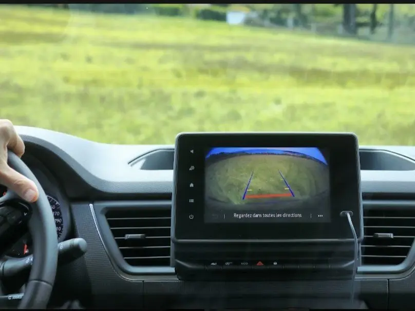 Vue intérieure centrée sur l'écran de la caméra de recul du Renault Trafic Fourgon gris, volant à gauche visible.