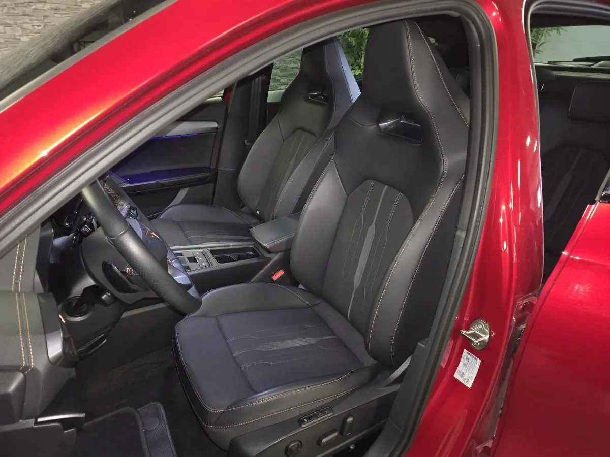 Vue intérieure côté conducteur du CUPRA Formentor 1.4 e-Hybrid 2024 rouge, sièges baquets noirs avec surpiqûres cuivre.