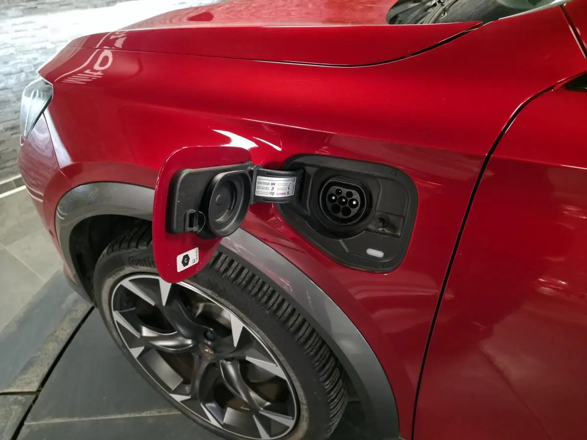 Vue rapprochée du côté gauche arrière du CUPRA Formentor rouge avec prise de recharge hybride ouverte et jante alliage 19 pouces.